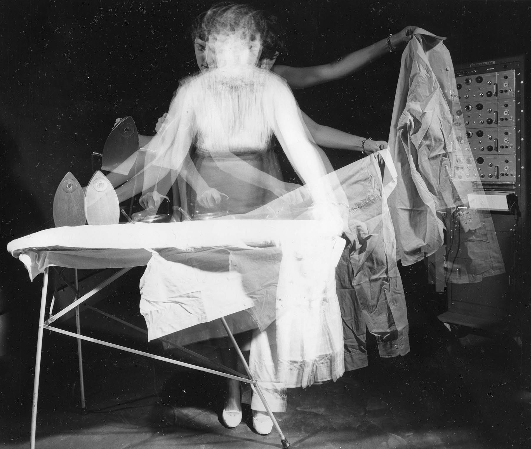 Woman ironing clothes on an ironing board. Image has a long exposure showing movement of the ironing